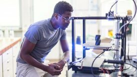 African-American male engineer using a 3D printer in the laboratory while studying a product prototype, and technology.