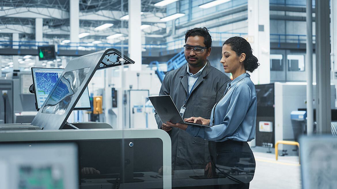 Male Industrial Engineer And Female Manager Using Laptop And Talking At Electronics Factory Male Industrial Engineer And Female Manager Using Laptop And Talking At Electronics Factory. The man is using a soldering jet printer.